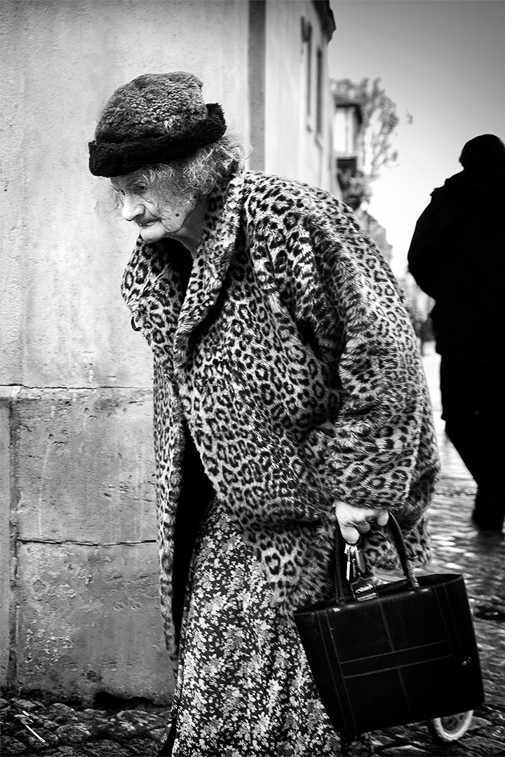 A woman wearing a hat and patterned coat carrying a handbag.